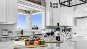 Una cocina moderna con armarios blancos, una isla grande con frutero, una botella de vino y copas.