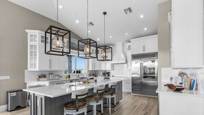 Una cocina moderna con una isla grande, taburetes de bar, iluminación colgante y electrodomésticos de acero inoxidable.