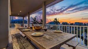 Mesa de madera lista para cenar con platos y copas de vino, con vistas a un paisaje urbano al atardecer.