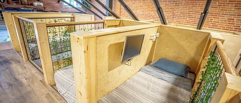 A wooden room with a bed, a small TV, and a window overlooking a brick wall.