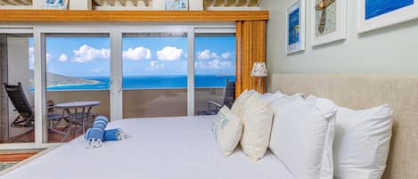 A hotel room with a large bed, a balcony with a view of the sea, and a dining area with a table and chairs.
