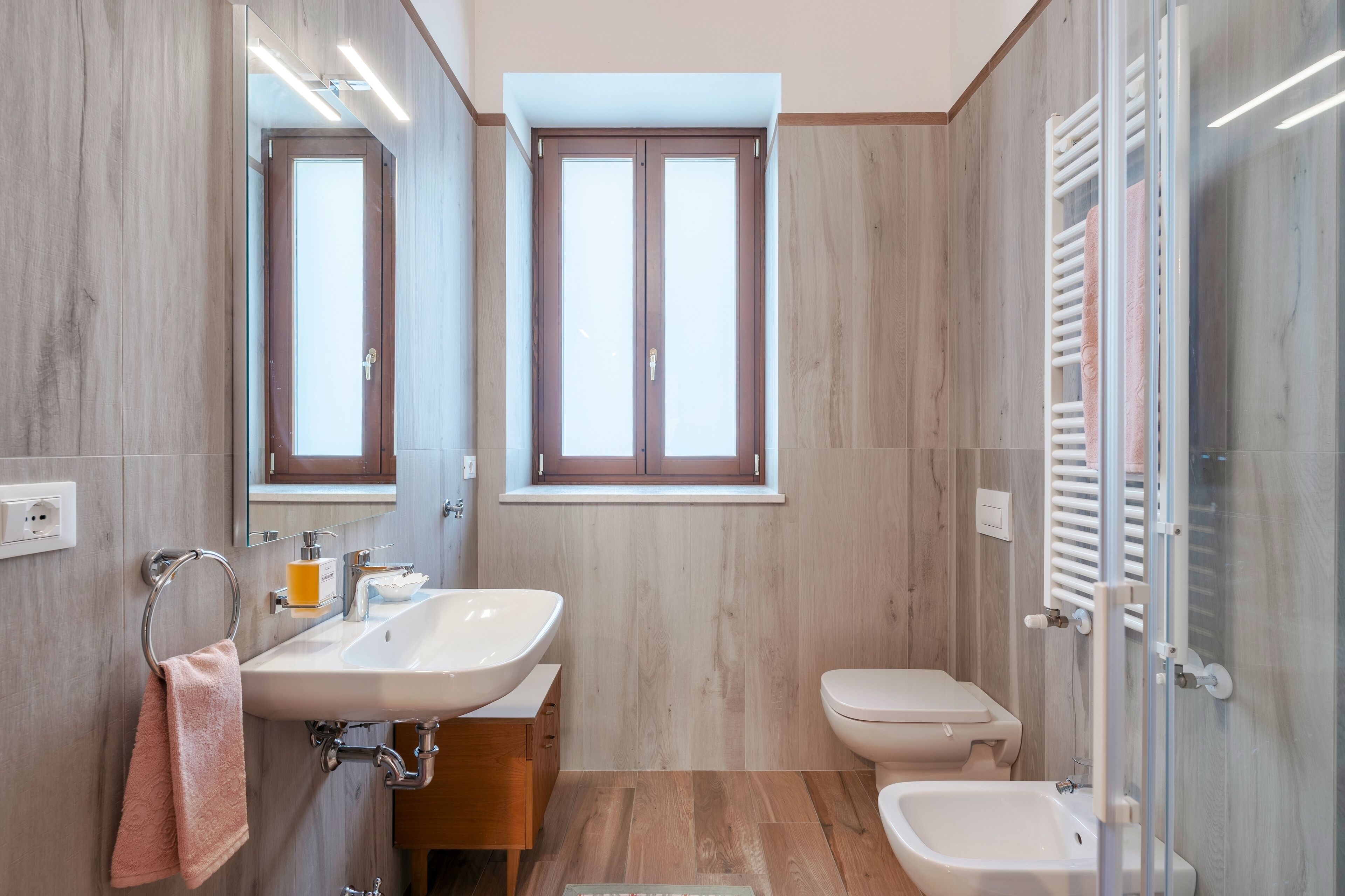 Un bagno moderno con un lavandino capiente, un water e un bidet. Sono presenti due finestre e un portasciugamani con asciugamani.