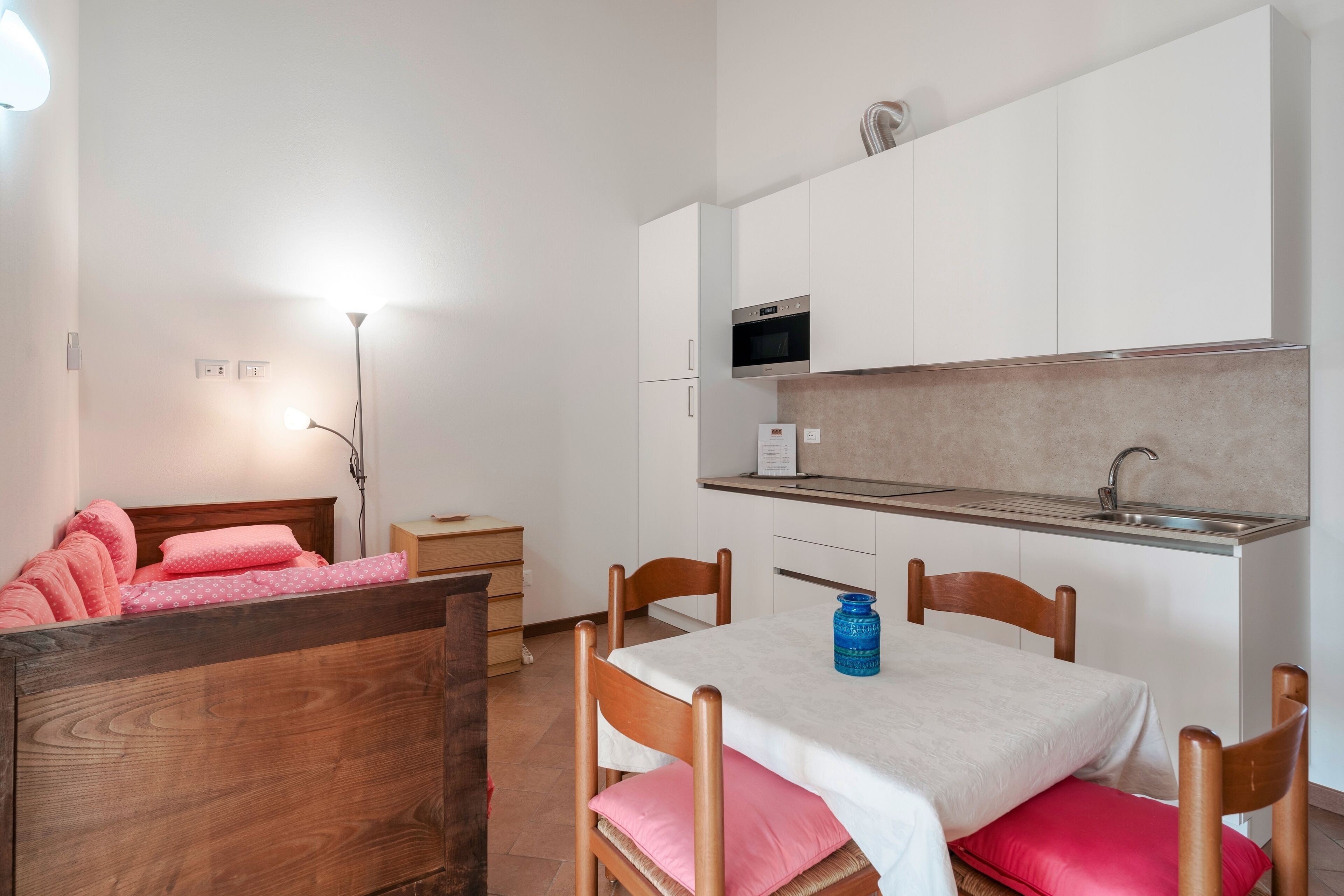 Habitació senzilla amb llit, taula petita i zona de cuina.