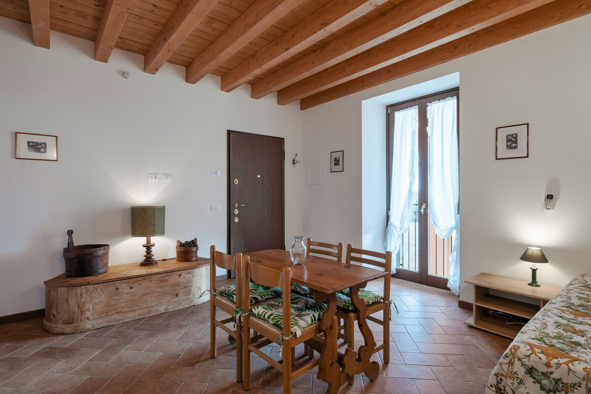 A wooden dining table with chairs, a wooden bench, a lamp, and a bed with a floral bedspread.
