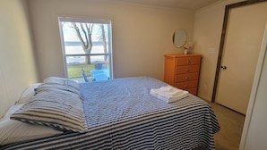 Un dormitorio con cama, cómoda, espejo y ventana con vistas al exterior.