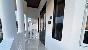 Un porche cubierto con columnas blancas, una puerta negra y un acceso con baldosas de piedra.