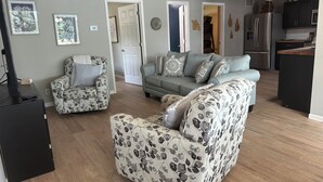 A living room with a sofa, armchair, and ottoman, a kitchen with appliances, and a ceiling fan. - Welcome to Rivers Edge Retreat – Your Serene Escape on the Osage River (Jefferson City)