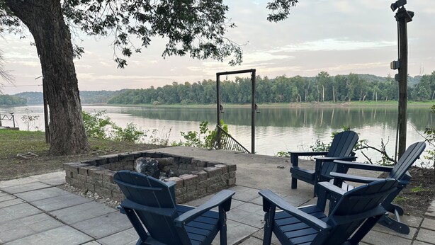 A lakeside patio with Adirondack chairs, a fire pit, and a view of the lake and forest. - Welcome to Rivers Edge Retreat – Your Serene Escape on the Osage River (Jefferson City)