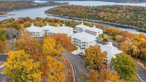 A large building with multiple wings, surrounded by autumn foliage and a lake.