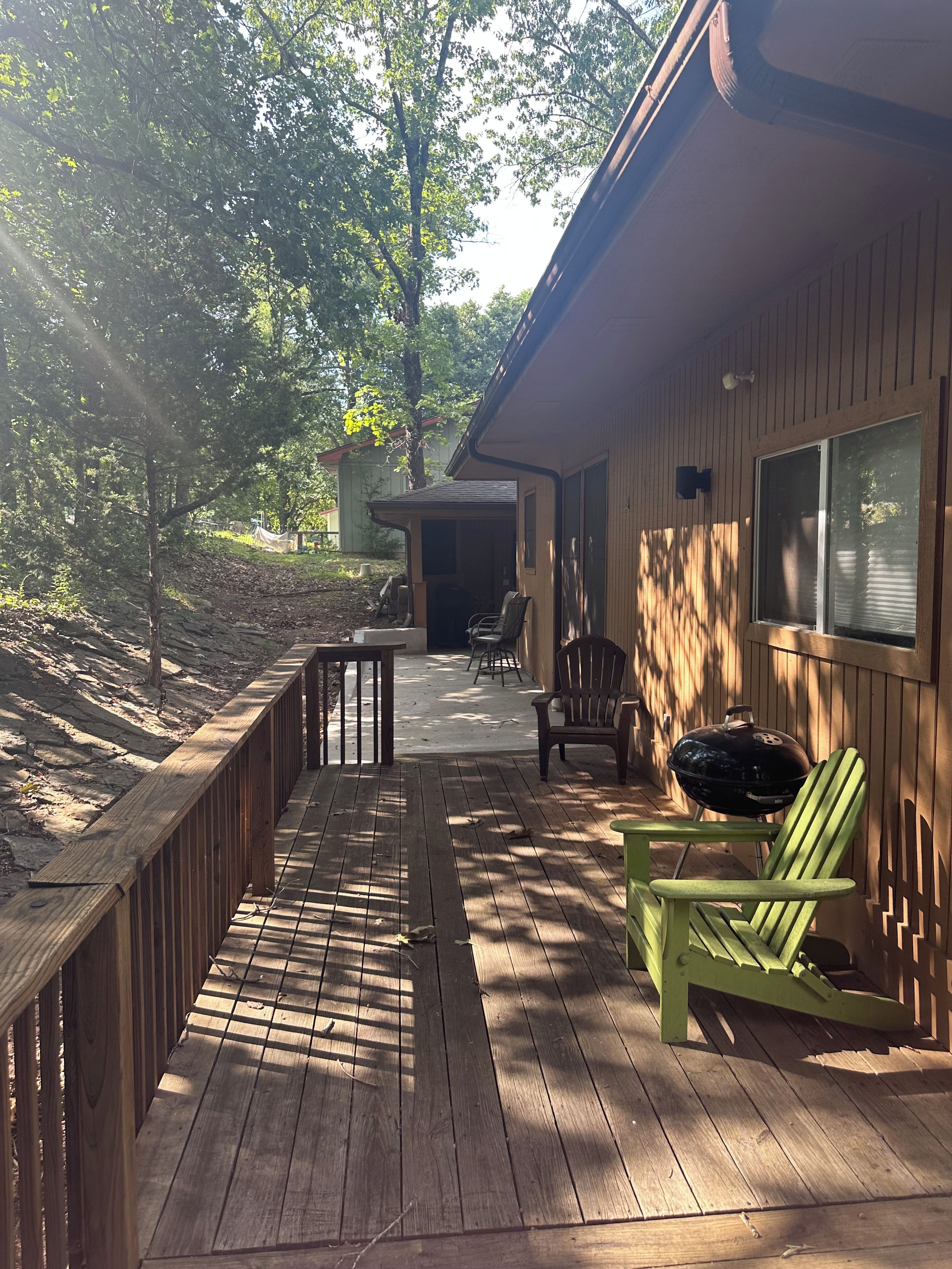 A wooden deck with a covered seating area, a grill, and a view of a forested area.