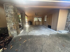 Un espace extérieur abrité, doté d’une colonne en pierre, d’un ventilateur de plafond et d’un sol en béton parsemé de feuilles.