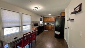 A compact kitchen with wooden cabinets, a black refrigerator, and a dining area with red chairs. - Cozy cabin in serene Bella Vista with WiFi and AC (Bella Vista)