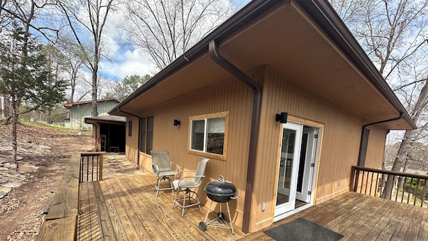 A wooden deck with a barbecue grill and two chairs, a covered patio area, and a house with a sliding glass door. - Cozy cabin in serene Bella Vista with WiFi and AC (Bella Vista)