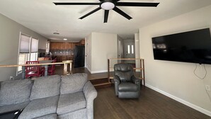 A living room with a gray sofa, a black leather chair, a ceiling fan, and a flat-screen TV mounted on the wall. - Cozy cabin in serene Bella Vista with WiFi and AC (Bella Vista)