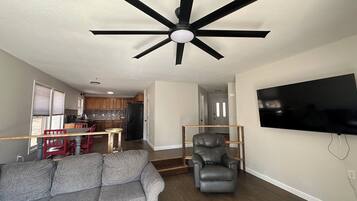 A living room with a gray sofa, a black leather chair, a ceiling fan, and a flat-screen TV mounted on the wall.