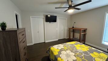 A bedroom with a bed, dresser, ceiling fan, TV, and a window.