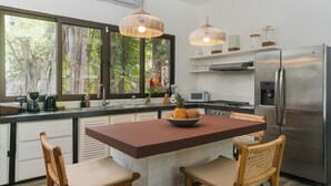 A modern kitchen with a central island, stainless steel appliances, and wicker chairs. - Oceano5, 4 bedroom Pool Villa - 4 min walk to the beach (nosara)