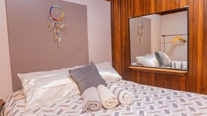 Een net opgemaakt bed met een bedsprei met patroon, een spiegel erboven en een dromenvanger aan de muur.