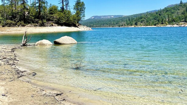 Un lac aux eaux limpides, bordé d’une plage de sable, entouré d’arbres et avec des collines en arrière-plan.
