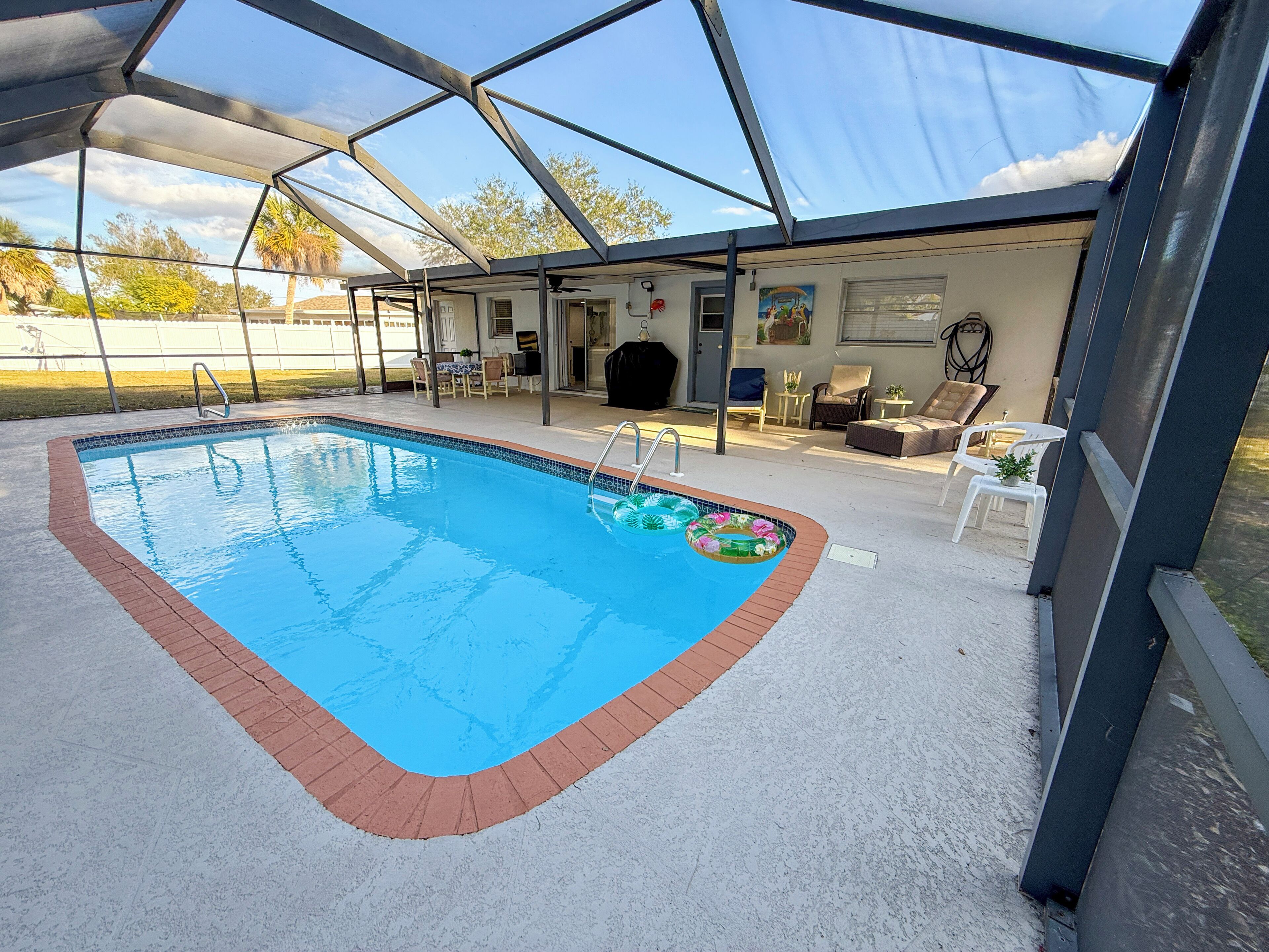 A covered swimming pool with a clear blue water feature, surrounded by a white tiled deck and a brick border.