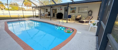 A covered swimming pool with a clear blue water feature, surrounded by a white tiled deck and a brick border.