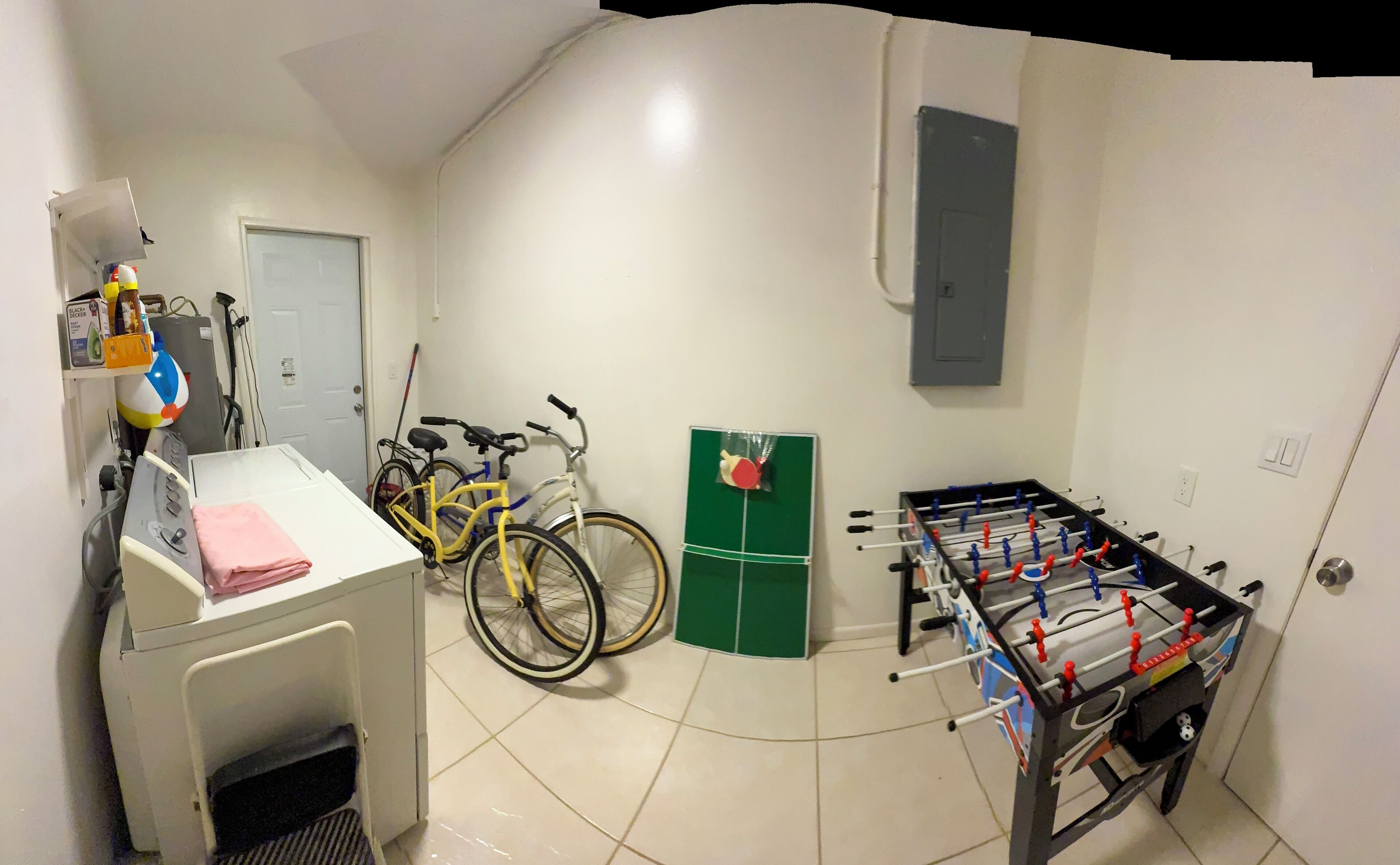 A room with a washing machine, a yellow bicycle, a green door, and a foosball table.
