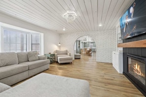 Un salon moderne avec une cheminée, un canapé, un coin repas et une cuisine visible à travers une arche.