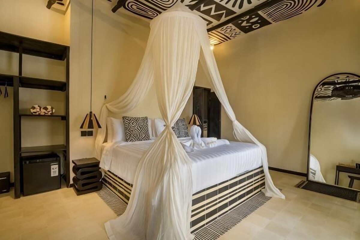 A four-poster bed with a canopy, a bedside table, a mirror, and a wardrobe.