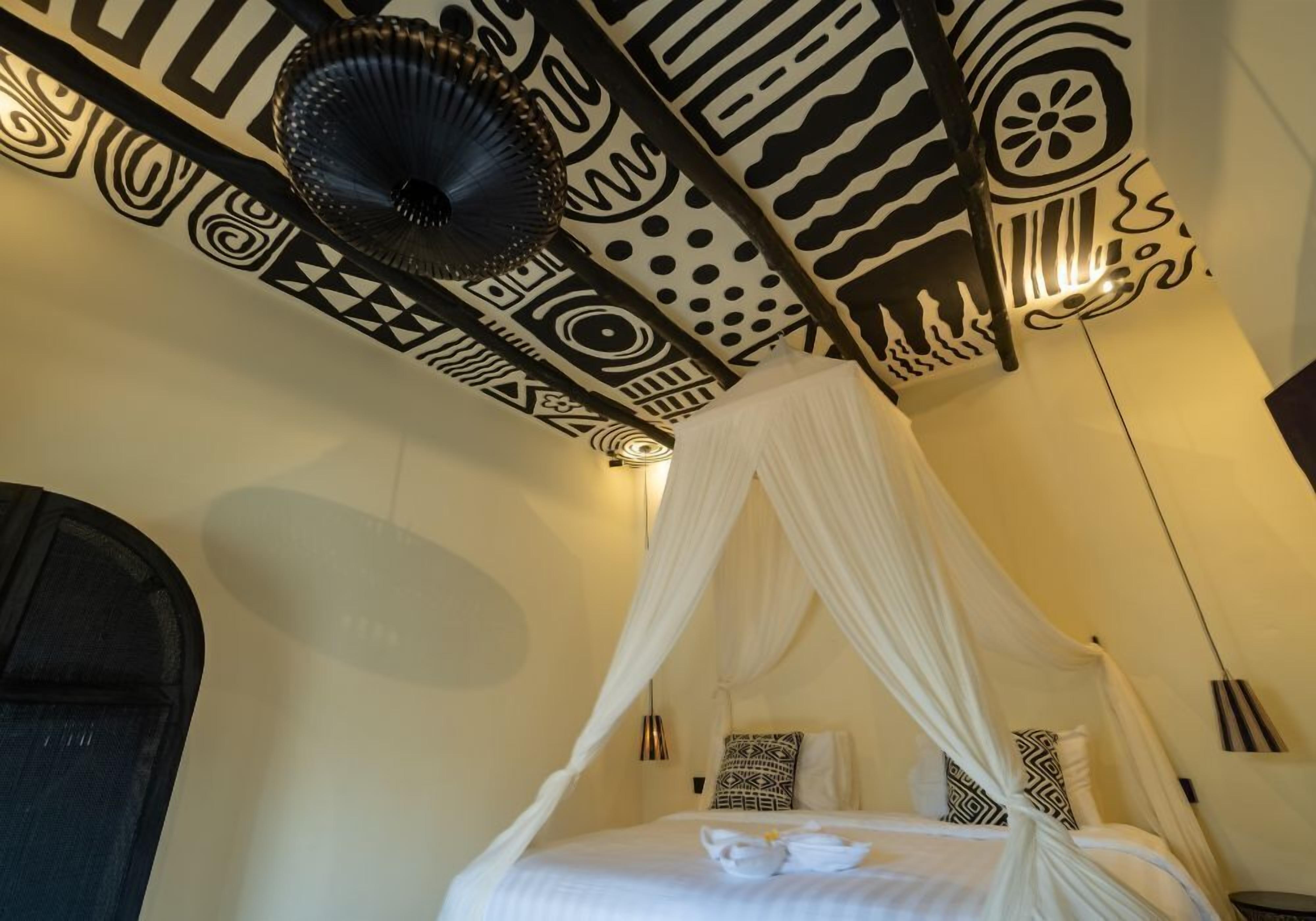 Une chambre avec un lit sous un dais blanc, des murs à motifs et un ventilateur de plafond noir.