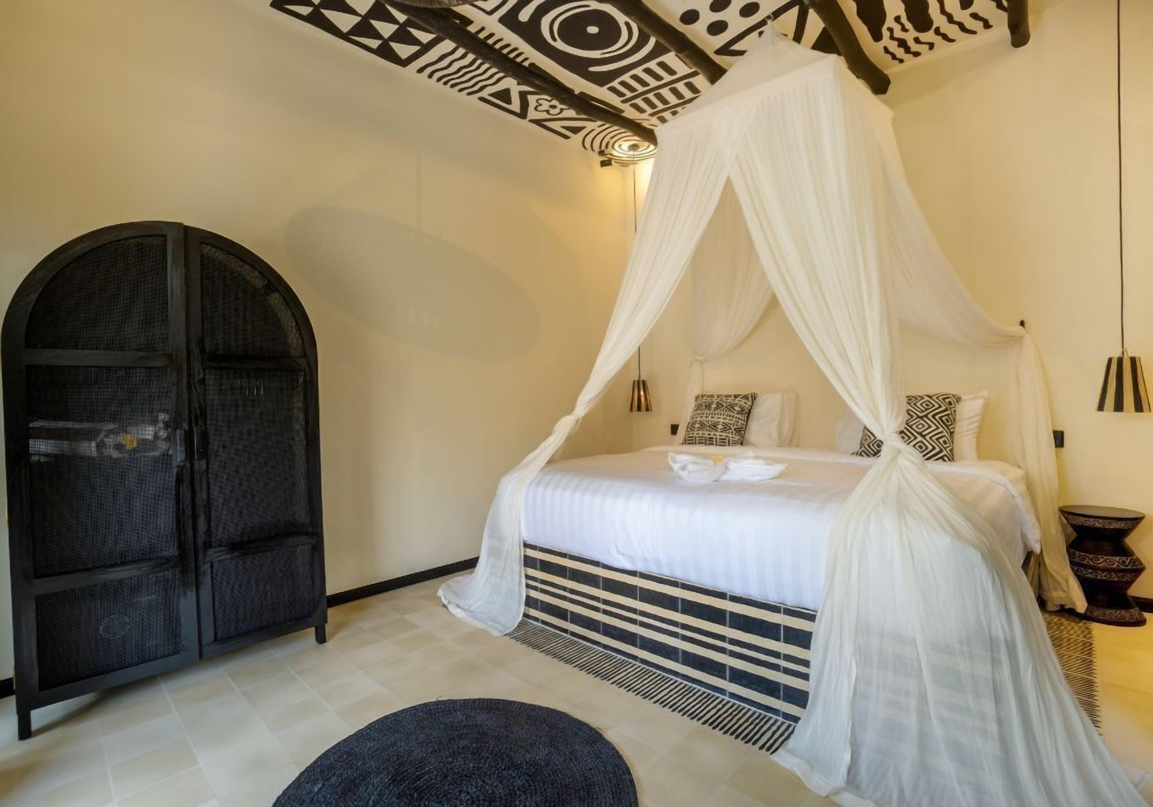 Un dormitorio con una cama bajo un dosel blanco, un armario arqueado negro y almohadas estampadas.