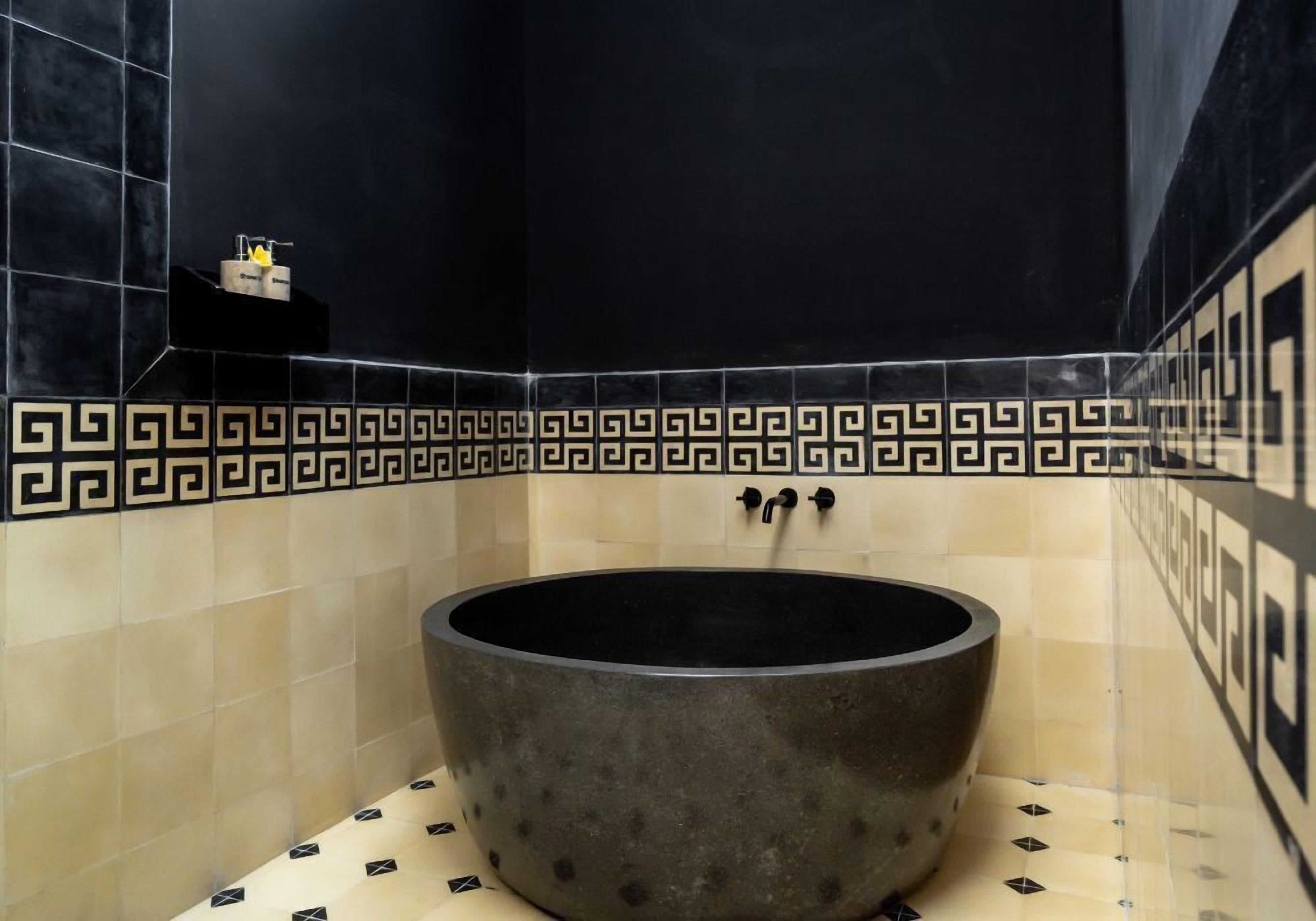 Un baño con una bañera independiente, baldosas negras y beige, y un borde decorativo.