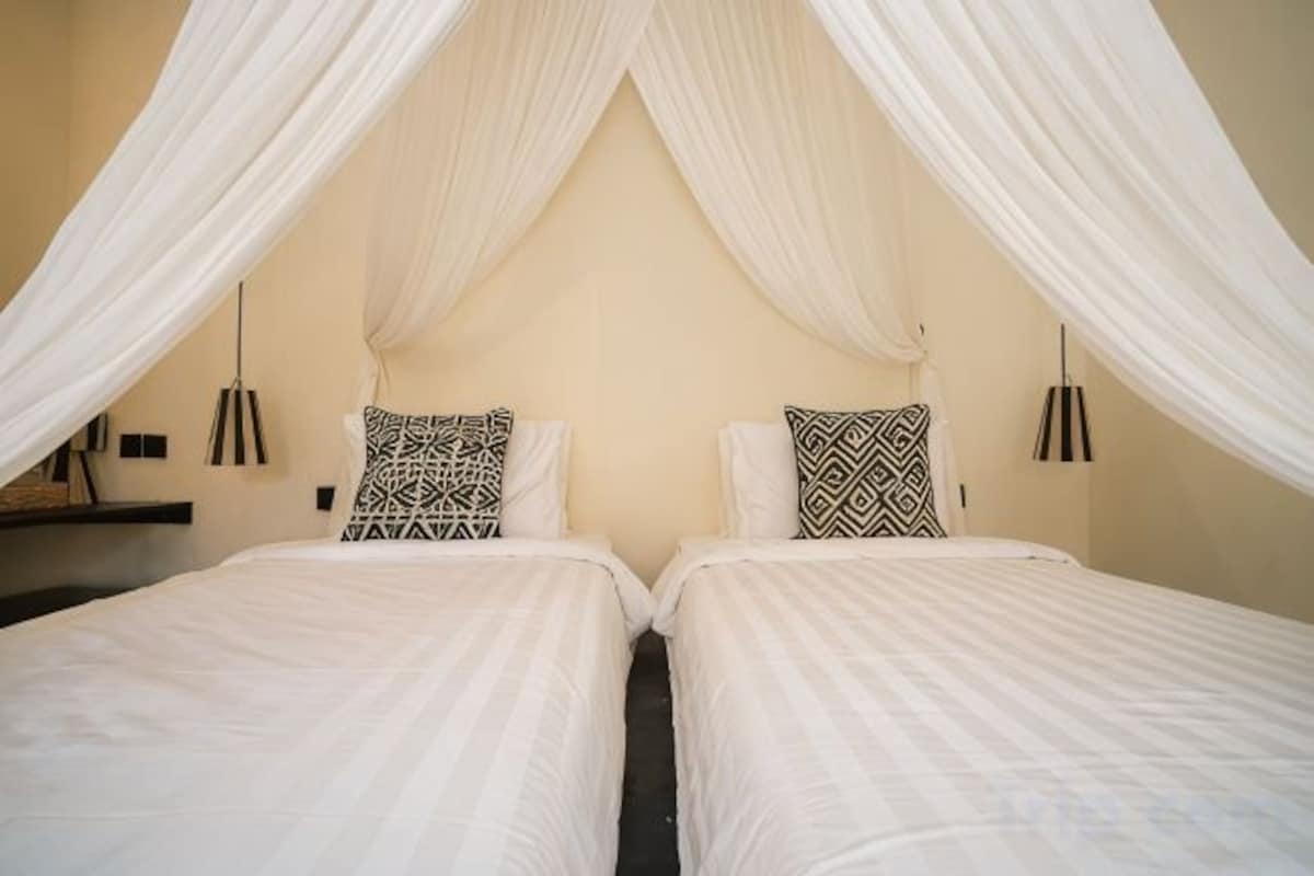 Una habitación con dos camas, cada una con una colcha blanca y un cojín estampado.