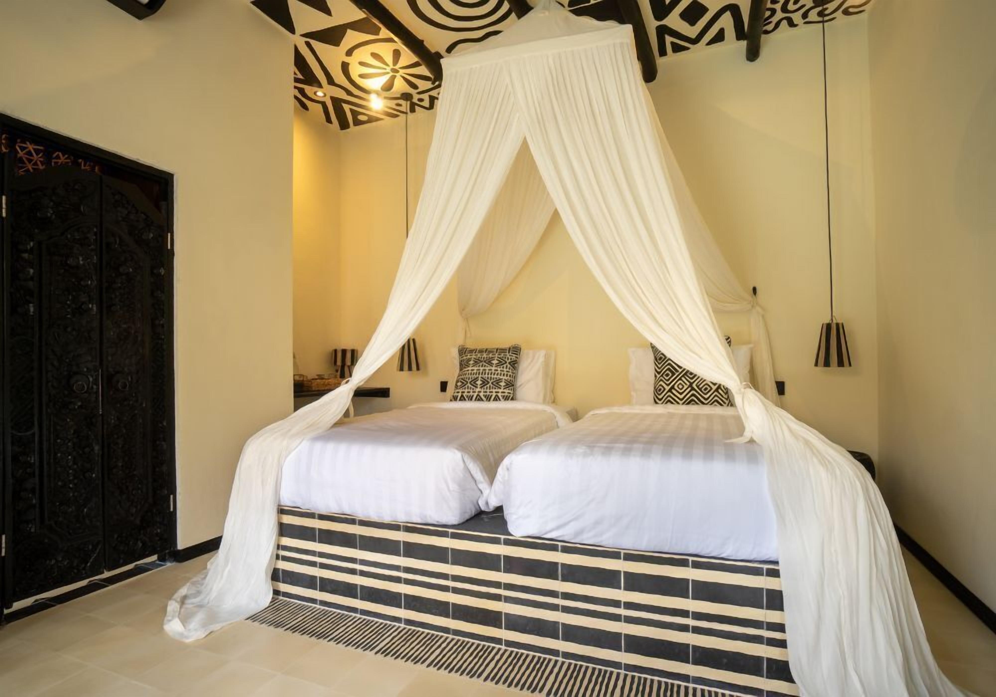 A room with a bed under a canopy, a patterned wall, and a black door.