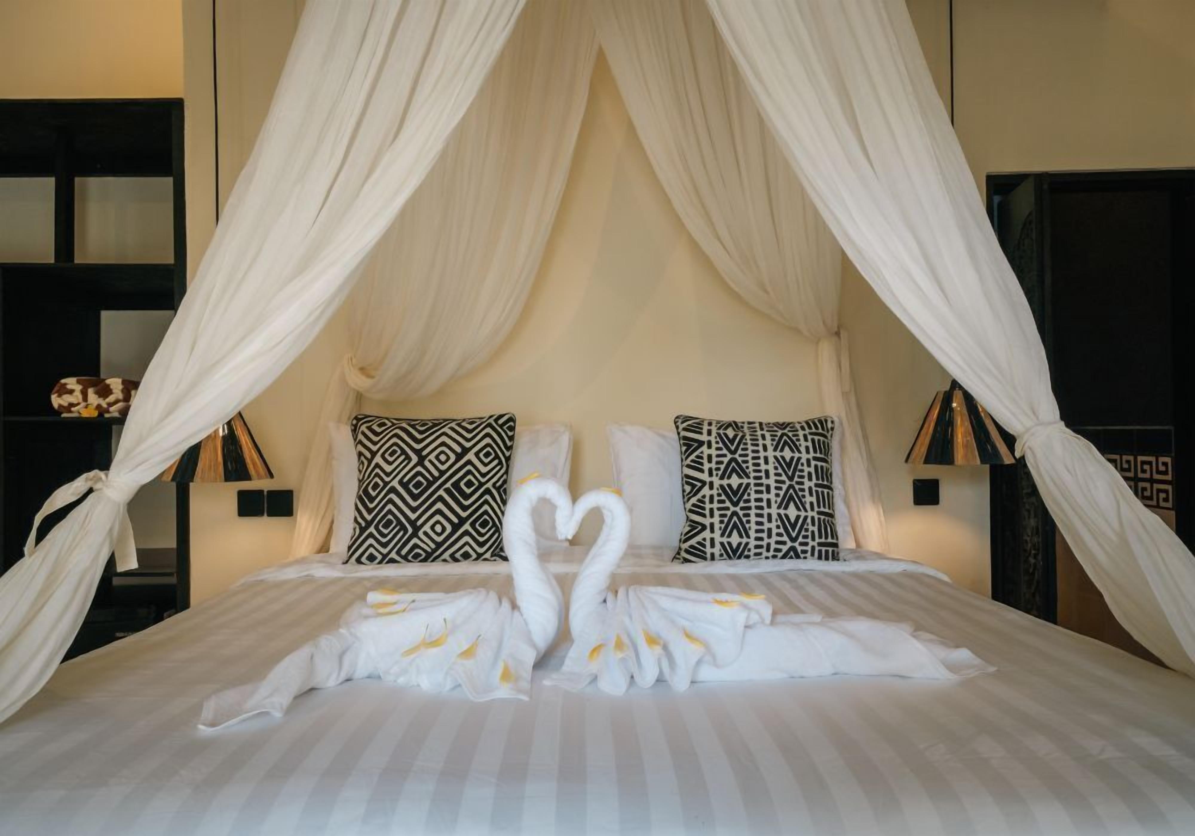 Ein Bett mit Baldachin, Kissen mit geometrischen Mustern und Handtücher in Schwanzform drapiert.