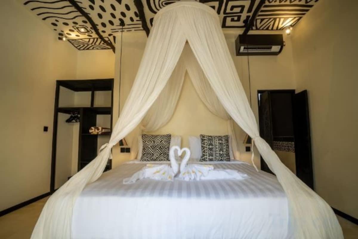Una cama con dosel, dos almohadas y una decoración con forma de cisne en la colcha.