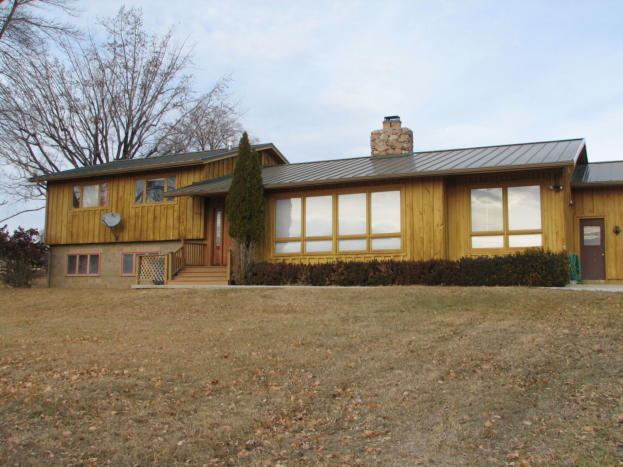 A two-story wooden building with a stone chimney, large windows, and a small porch.
