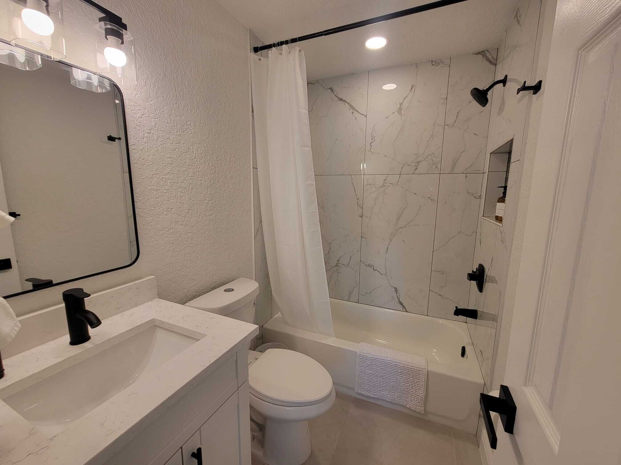 A modern bathroom with a white marble shower, a white toilet, and a sink with a mirror above it.