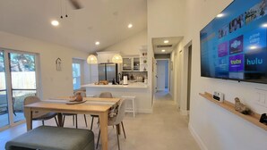 Una cocina moderna con armarios blancos, una isla central y un comedor con mesa y sillas de madera.