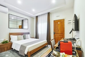 A hotel room with a bed, a desk with a computer, a chair, a TV, and a mirror.