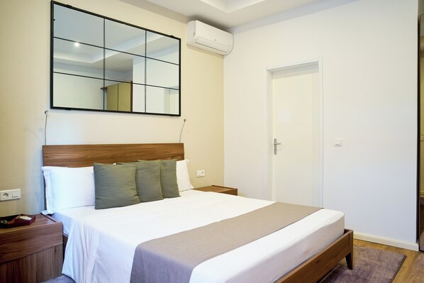 A bedroom with a large bed, a nightstand, a mirror, and a door. - Roma Hôtel & Restaurant (Libreville)