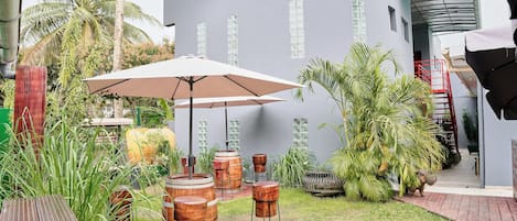 Un patio con una mesa de madera, un paraguas grande y varios taburetes de madera.