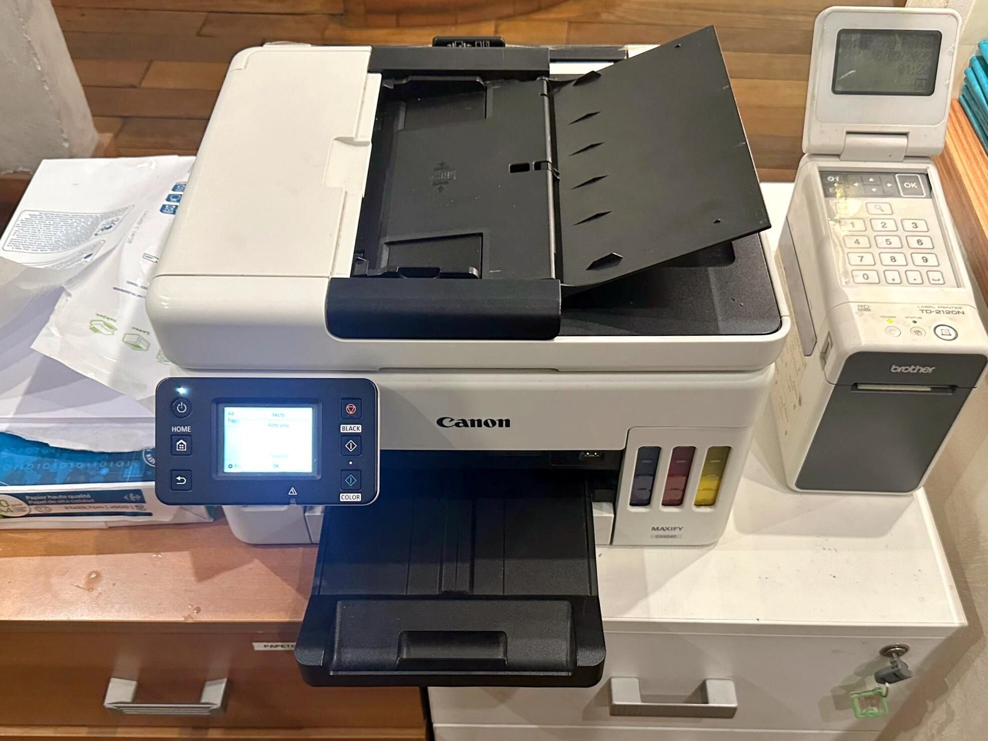 A Canon printer with a control panel, a paper tray, and a label printer on top.