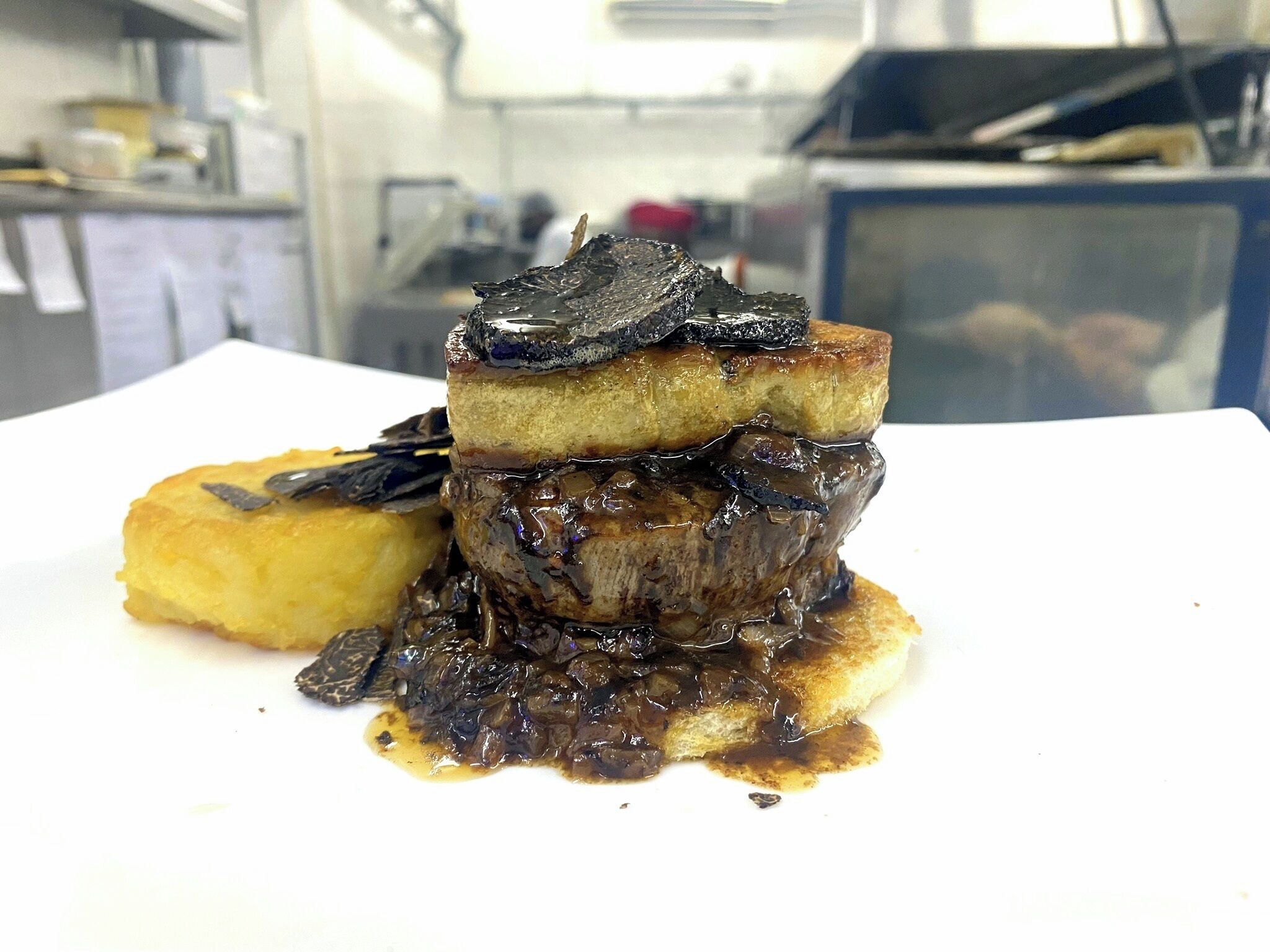 A dish with a stack of food items, possibly including a piece of meat and a side of fruit or vegetable.