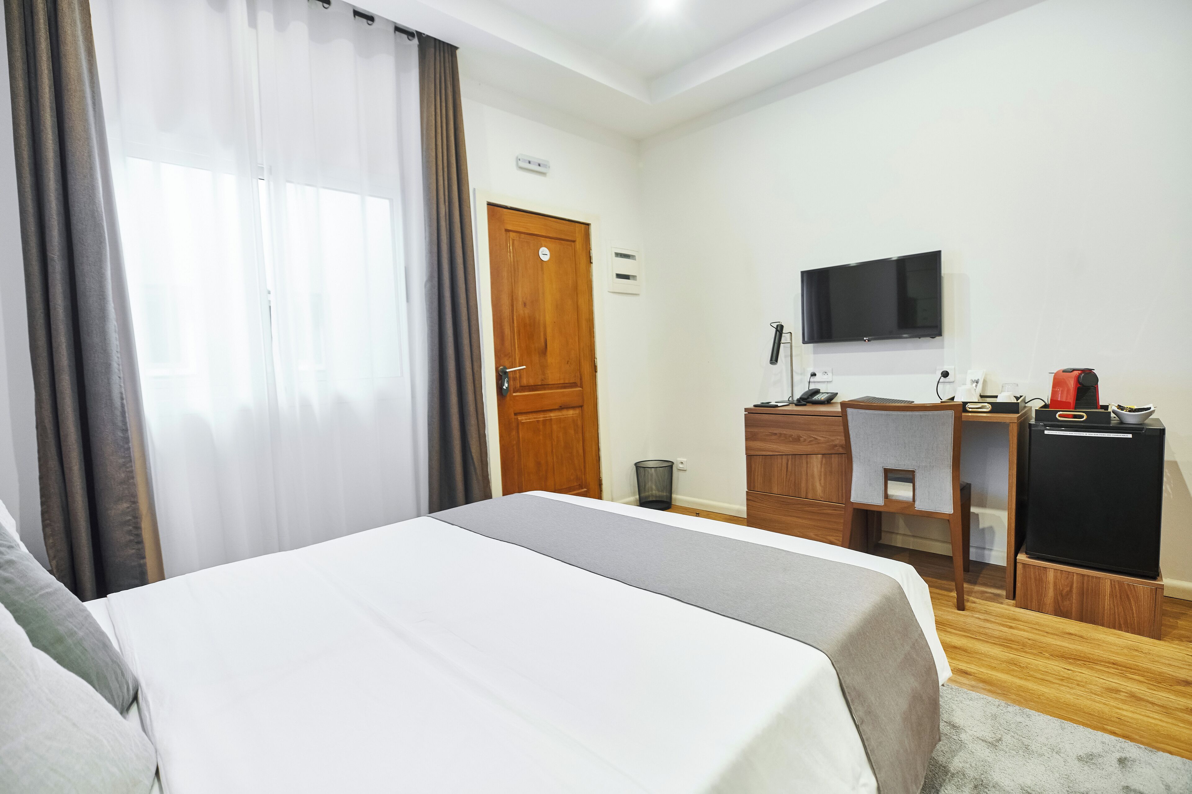 A hotel room with a bed, a desk, a TV, and a refrigerator.