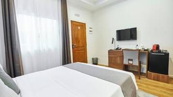 A hotel room with a bed, a desk, a TV, and a refrigerator.