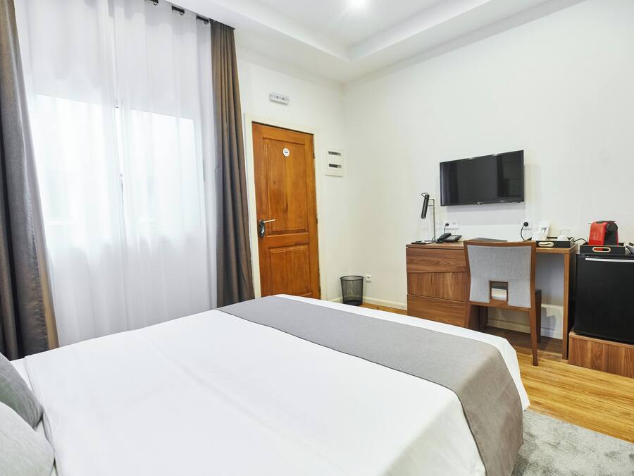 A hotel room with a bed, a desk, a TV, and a refrigerator.