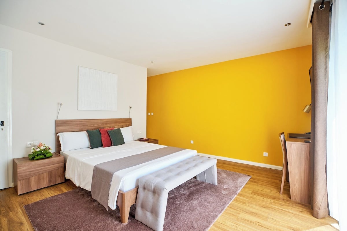 Ein Schlafzimmer mit einem Bett, Nachttischen, einer Bank, einem Schreibtisch und einem Stuhl.