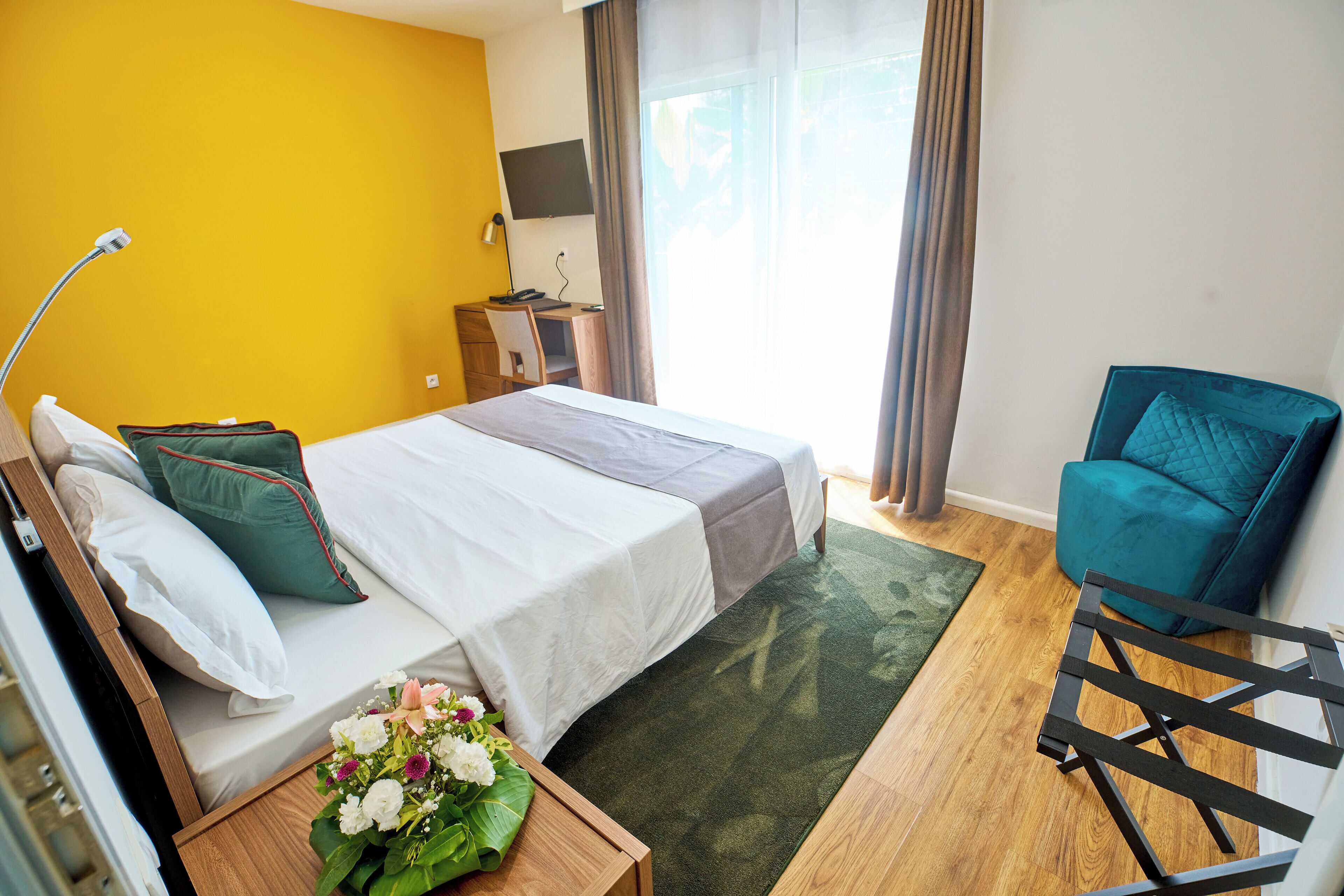 Une chambre d’hôtel avec un lit, un bureau, une chaise et un téléviseur fixé au mur.