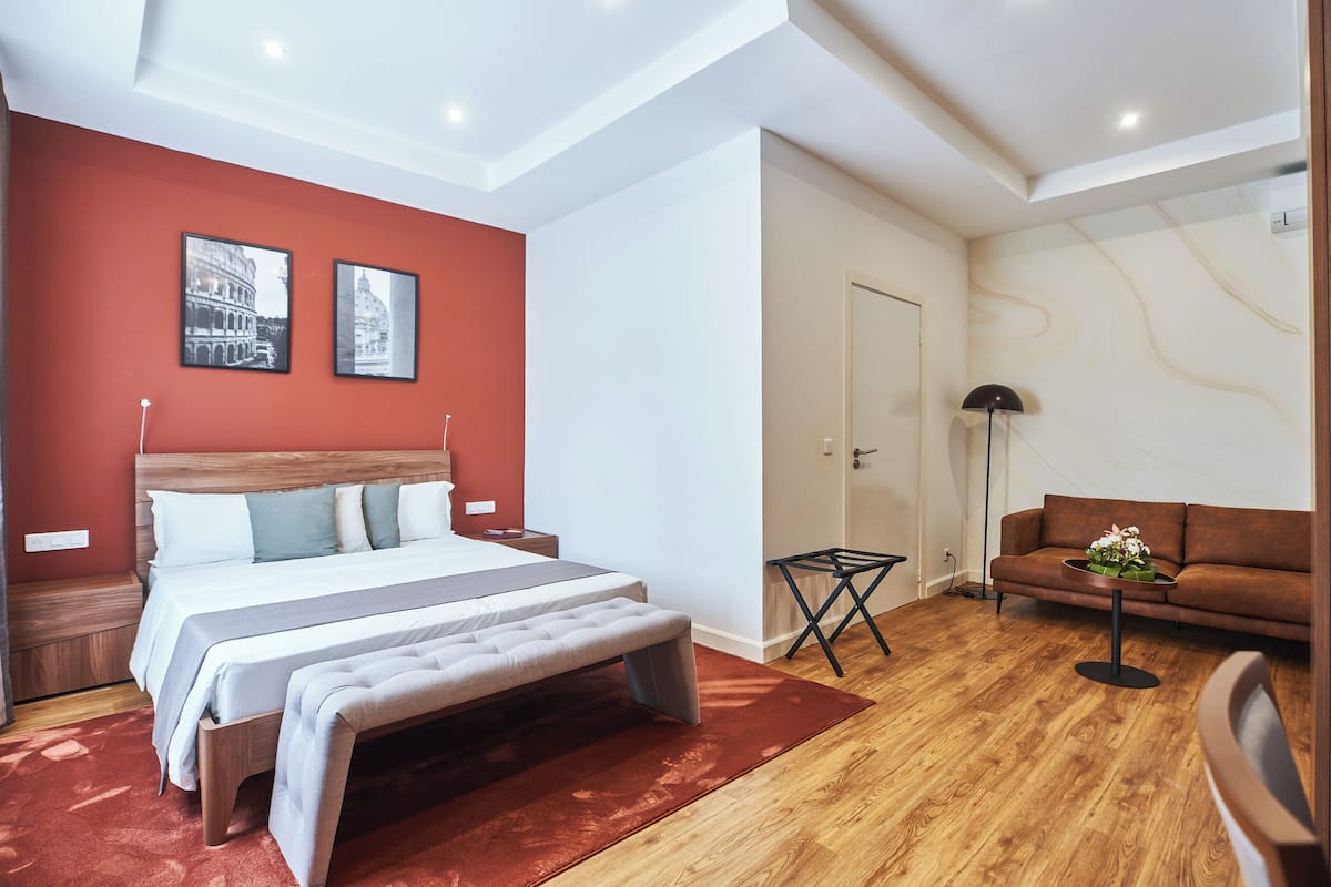 Ein modernes Schlafzimmer mit einem großen Bett, einer Bank, einer Couch und einem kleinen Tisch mit Blumen.