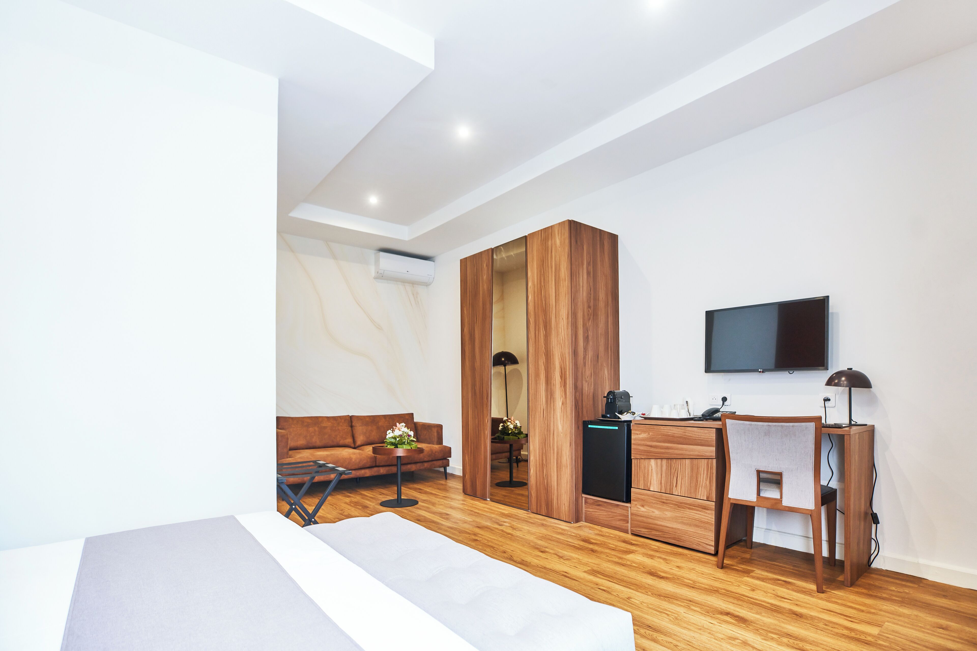 Un dormitorio moderno con cama, armario de madera, escritorio con silla, televisor y sofá.